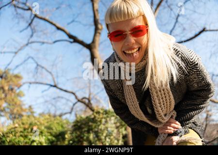 Jeune fille hippie amusante heureuse montrant la langue à la caméra pour le plaisir et faire des visages drôles tout en portant des lunettes de soleil fraîches. Femme féminine attrayante appréciant Banque D'Images