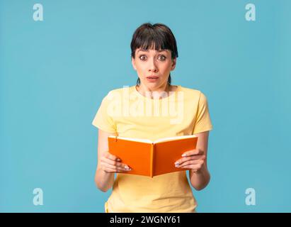 étudiante malheureuse tenant un portrait isolé à livre ouvert sur fond bleu. Concept d'étude et d'apprentissage Banque D'Images