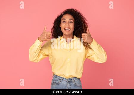Femme noire souriante donnant deux pouces sur fond rose Banque D'Images