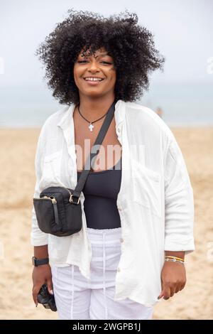 Portrait d'une jeune femme noire sur la plage, elle sourit à la caméra Banque D'Images