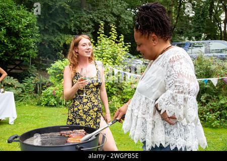 Femmes appréciant une fête de jardin barbecue d'été cuisiner et manger à l'extérieur Banque D'Images