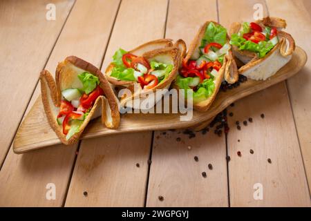 Salade avec tartelettes sur une planche sur une table en bois. Les tartelettes sont faites à partir de pain grillé. Ustensiles alimentaires comestibles. Banque D'Images