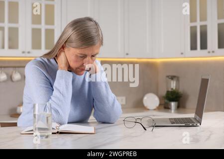 Ménopause. Femme souffrant de douleur dans le cou à table dans la cuisine, espace pour le texte Banque D'Images