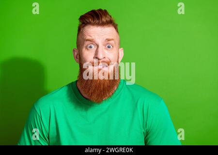 Portrait de gars nerveux inquiet sans voix avec barbe rouge porter un t-shirt élégant fixant des lèvres mordantes isolées sur fond de couleur verte Banque D'Images