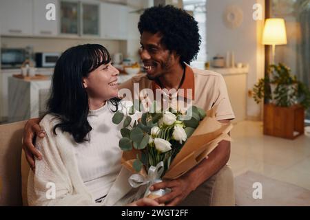 Jeunes rencontres souriantes interculturelles se regardant tandis que l'afro-américain embrassant sa petite amie tenant un bouquet de fleurs Banque D'Images
