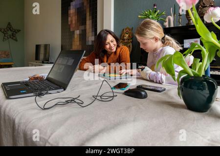 Jeune petite-fille adolescente aidant une femme âgée à faire des recherches et à remplir le formulaire avec son ordinateur portable et son téléphone. Famille autour de la soutenir Banque D'Images