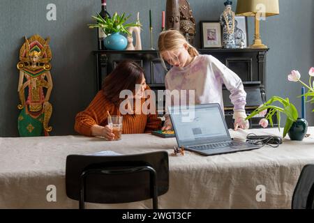 Jeune petite-fille adolescente aidant une femme âgée à faire des recherches et à remplir le formulaire avec son ordinateur portable et son téléphone. Famille autour de la soutenir Banque D'Images