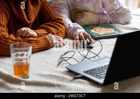 Jeune petite-fille adolescente aidant une femme âgée à faire des recherches et à remplir le formulaire avec son ordinateur portable et son téléphone. Famille autour de la soutenir Banque D'Images