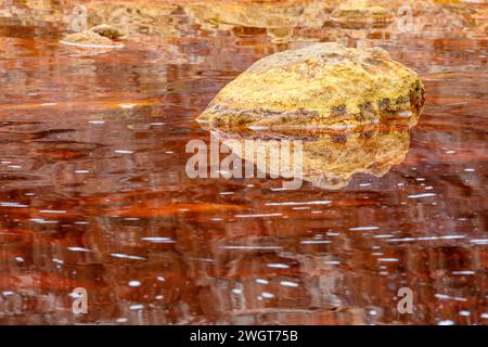 Un rocher doré solitaire jette son reflet sur les eaux rouges tranquilles et riches en fer du Rio Tinto Banque D'Images