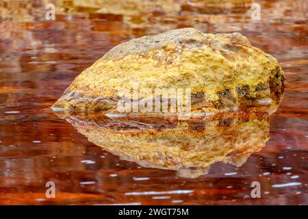 Un rocher doré solitaire jette son reflet sur les eaux rouges tranquilles et riches en fer du Rio Tinto Banque D'Images