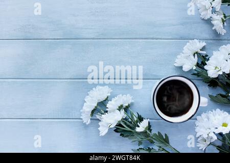 Tasse de café chaud en émail entouré de fleurs blanches de chrysanthème sur une table rustique bleue. Vue de dessus de table. Directement au-dessus. Banque D'Images