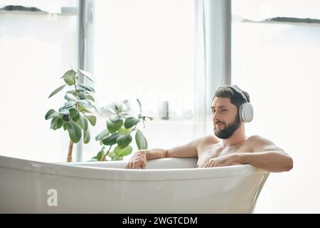 joyeux homme avec barbe et écouteurs assis et relaxant dans sa baignoire, santé mentale Banque D'Images