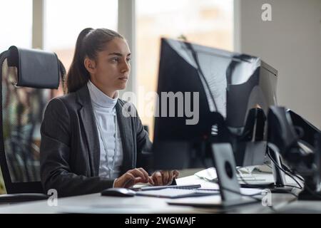 Portrait de vue latérale d'une jeune femme développeur INFORMATIQUE utilisant un ordinateur dans un espace de copie minimal sur le lieu de travail de bureau Banque D'Images