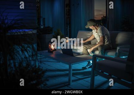 Homme caucasien travaillant à distance sur un ordinateur portable depuis son patio assis à côté de son chien Banque D'Images