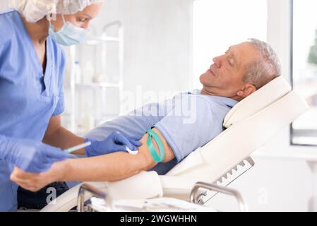 Homme senior allongé sur le canapé, obtenant une injection intraveineuse au cabinet médical Banque D'Images