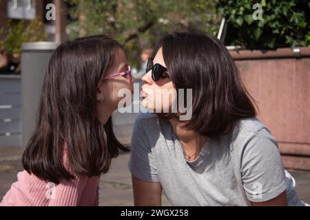 Mère et fille en lunettes de soleil assis dans la rue et se regardant Banque D'Images