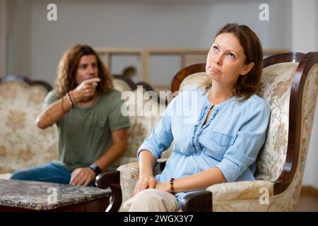 Couple décontracté bouleversé parlant dans des tons élevés les uns avec les autres tout en étant assis sur le canapé dans le salon Banque D'Images