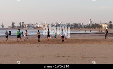 Des jeunes hommes jouent au football sur une plage de sable un soir avec la médina historique derrière à Essaouira, Maroc, le 6 février 2024 Banque D'Images