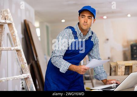 Un technicien vérifie les documents et utilise un ordinateur portable pendant les travaux de réparation Banque D'Images