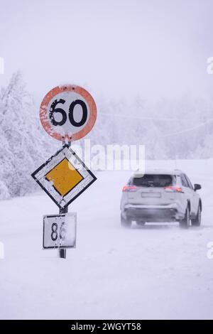 Voiture passant une vitesse de 60 km/h et panneaux routiers prioritaires dans des conditions de conduite glacées sur une autoroute à Senja, Norvège, Scandinavie, Europe Banque D'Images