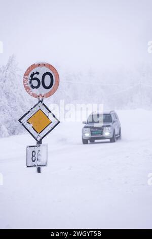 Véhicule 4x4 passant une vitesse de 60 km/h et panneaux routiers prioritaires dans des conditions de conduite glacées sur une autoroute à Senja, Norvège, Scandinavie, Europe Banque D'Images