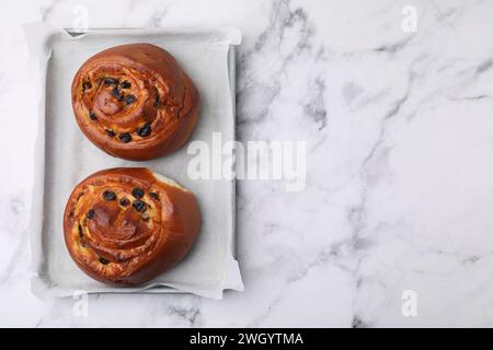 Délicieux rouleaux avec des raisins secs sur une table en marbre blanc, vue de dessus et espace pour le texte. Petits pains sucrés Banque D'Images