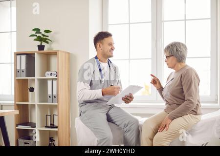 Jeune médecin heureux, infirmier masculin et vieille femme parlant, expliquant, prenant des soins sociaux Banque D'Images