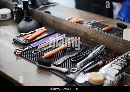 Vue rapprochée des outils du coiffeur. Photo recadrée de l'équipement du barbier sur la table en bois. Différents peignes et brosses reposant sur le fond du miroir. Banque D'Images