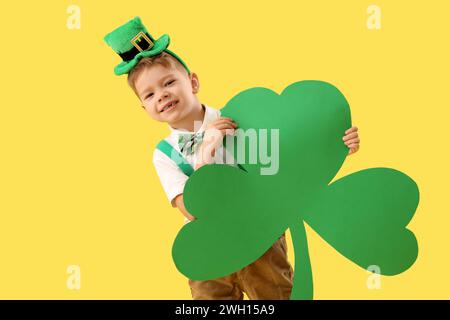 Petit garçon mignon avec chapeau de leprechaun et feuille de trèfle en papier sur fond jaune. Prog Célébration de la fête de Patrick Banque D'Images