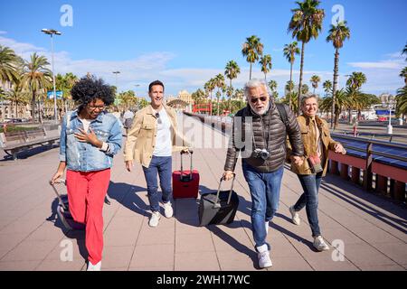 Groupe de quatre touristes multiraciaux d'âge moyen courant avec leurs bagages dans la rue. Banque D'Images