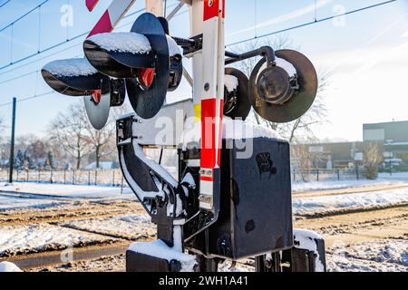 Gros plan des feux d'avertissement et des barrières de franchissement surélevées au passage à niveau, des voies ferrées recouvertes de neige en arrière-plan flou, journée ensoleillée après Heavy sno Banque D'Images