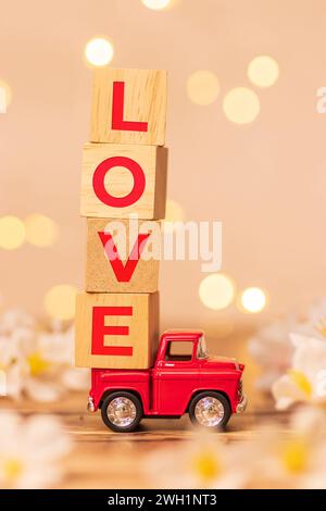 Rouge camion jouet transportant cube en bois avec texte amour à l'arrière du pick-up pour livrer l'amour pour la Saint-Valentin avec flou champ de fleurs blanches Banque D'Images