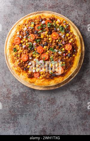 Pizza mexicaine épicée maison Taco avec bœuf haché, tomates, maïs, haricots noirs, fromage cheddar, oignon rouge sur la planche de bois sur la table. Vertical Banque D'Images