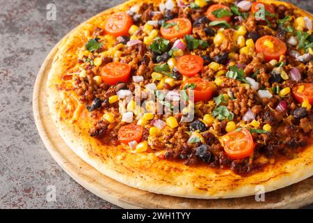 Pizza épicée mexicaine Taco avec bœuf haché, tomates, maïs, haricots noirs, fromage cheddar, oignon rouge sur la planche de bois sur la table. Horizontal Banque D'Images