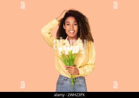 Femme noire joyeuse tient un bouquet de tulipes blanches sur fond beige Banque D'Images