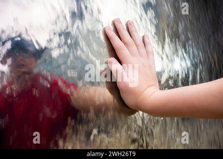 Sheffield, Royaume-Uni – 13 novembre 2021 : gros plan sur la main d’un adolescent touchant l’eau qui coule sur l’une des sphères argentées de la sculpture de pluie Banque D'Images