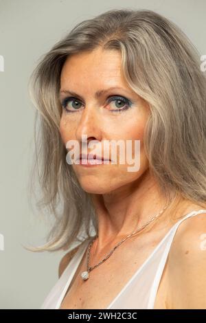Belle femme de cinquante ans aux cheveux gris regardant la caméra isolée sur fond gris. Mature vieille dame gros plan portrait. Le visage d'une femme vieillissante Banque D'Images