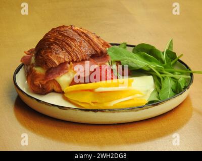 Un brunch composé d’un sandwich chaud au croissant avec jambon de Parme et fromage artisanal. Banque D'Images