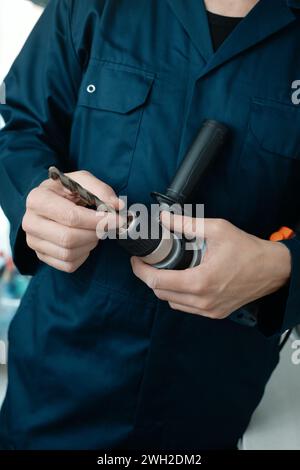 un homme caucasien, portant une combinaison bleue, met un foret métallique dans une perceuse électrique Banque D'Images