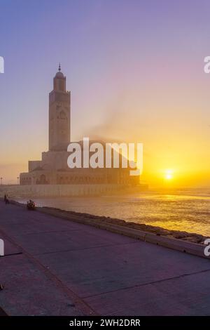 Vue sur le coucher du soleil de la mosquée Hassan II, avec la promenade et le phare El Hank, à Casablanca, Maroc Banque D'Images