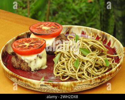 Délicieux filet mignon accompagné d'une salade caprese et servi avec des spaghettis nappés d'une délicieuse sauce pesto Banque D'Images