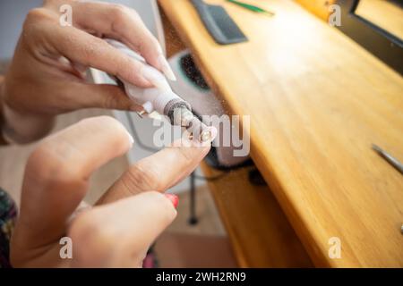 Gros plan photo d'une femme enlevant le vernis à ongles semi-permanent de ses ongles avec la roue de papier de verre. Banque D'Images