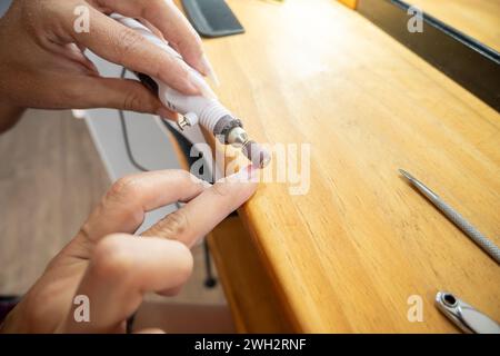 Gros plan photo d'une femme enlevant le vernis à ongles semi-permanent de ses ongles avec la roue de papier de verre. Banque D'Images