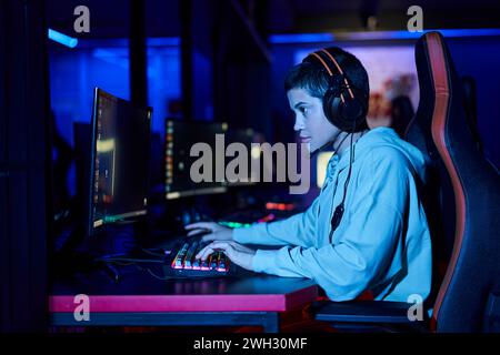 focus sur la jeune femme concentrée jouant au jeu dans une pièce éclairée bleue, joueur féminin cybersport Banque D'Images