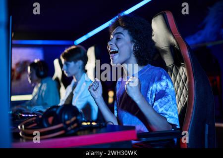 femme afro-américaine excitée regardant l'écran d'ordinateur et acclamant dans la salle éclairée bleue, gagnant Banque D'Images
