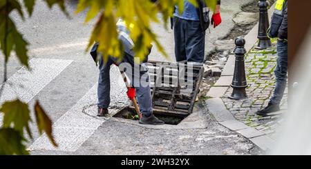 Groupe de travailleurs méconnaissables réparent la rue, effectuant des tâches pour entretenir et améliorer la route et le drainage des eaux usées. Banque D'Images