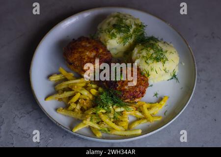 Cuisine polonaise classique : hamburgers hachés de porc, purée de pommes de terre, haricots jaunes, chapelure, garnie d'aneth finement haché. Banque D'Images