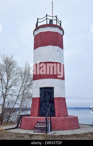 Petit phare peint en bandes rouges et blanches avec porte noire. Bâtiment à Novosibirsk, ville russe, Sibérie, OB mer, rivière. Destination touristique Banque D'Images