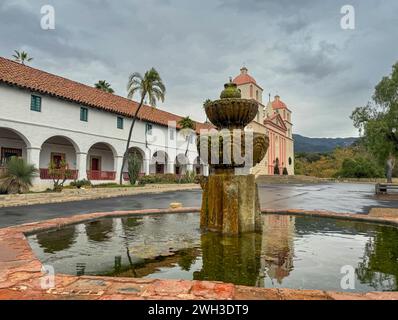 Santa Barbara, CA, États-Unis - 18 décembre 2023 : paysage, fontaine mauresque sur le côté du bâtiment de l'église Old Mission sous le ciel gris-bleu. Réflexion dans Wate Banque D'Images