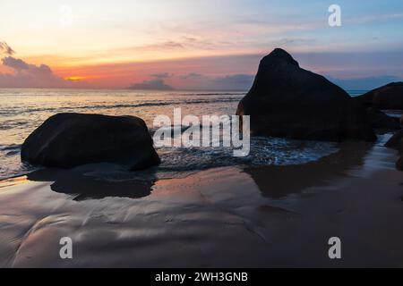 Beau Vallon Beach paysage balnéaire avec sable humide et silhouettes de rochers côtiers sur le coucher du soleil. Île de Mahé, Seychelles Banque D'Images